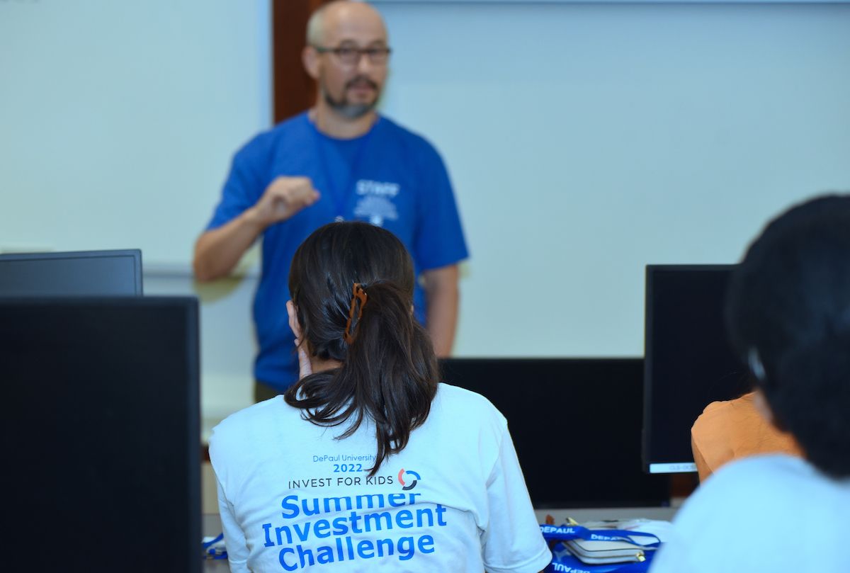 Student sitting in classroom during the 2022 Summer Investment Challenge. Photo shows back of student's t-shirt that says, "Summer Investment Challenge," while they listen to Professor Vahap Uysal teach in front of classroom.