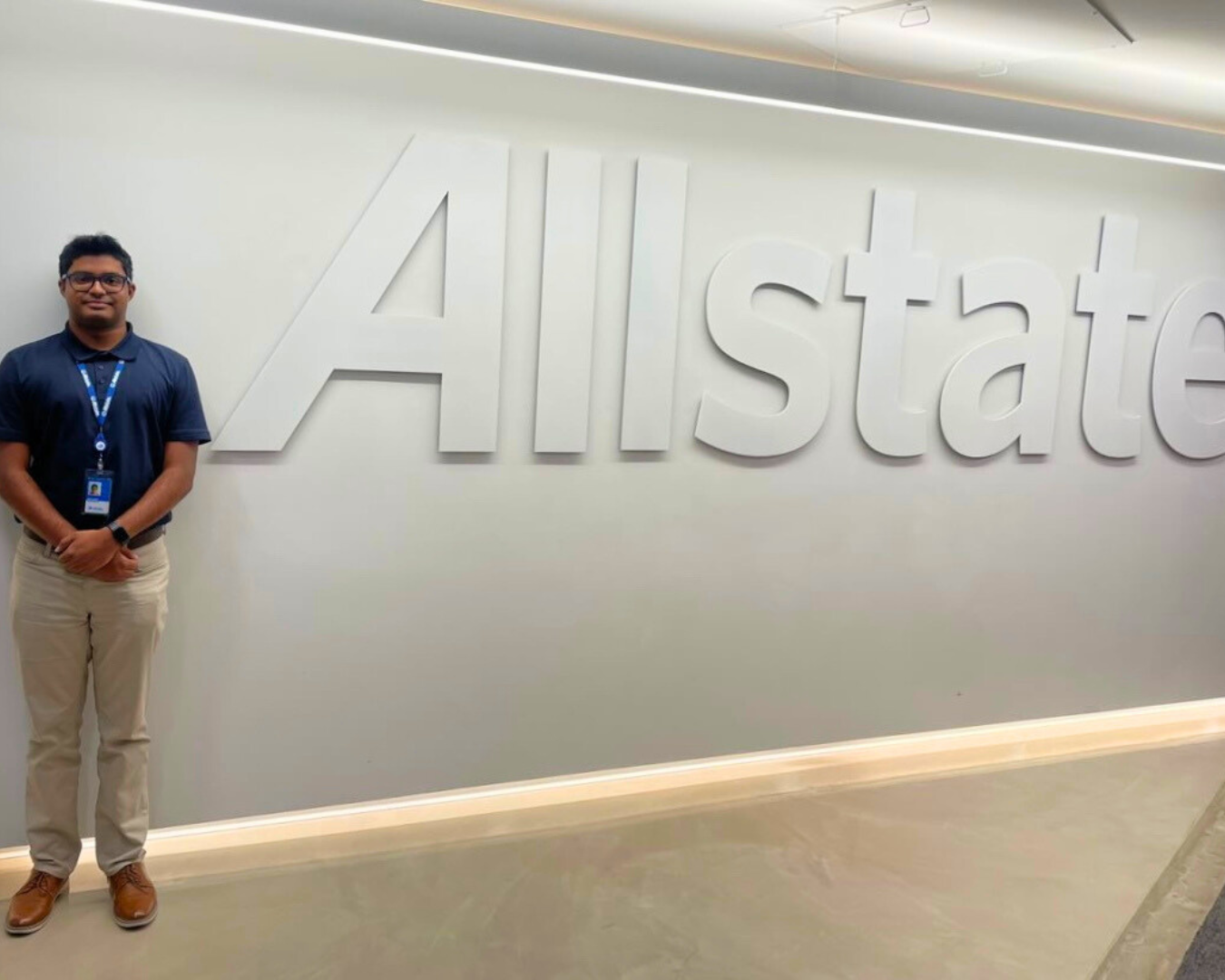 A young man posing in front of an office wall with the Allstate logo on it