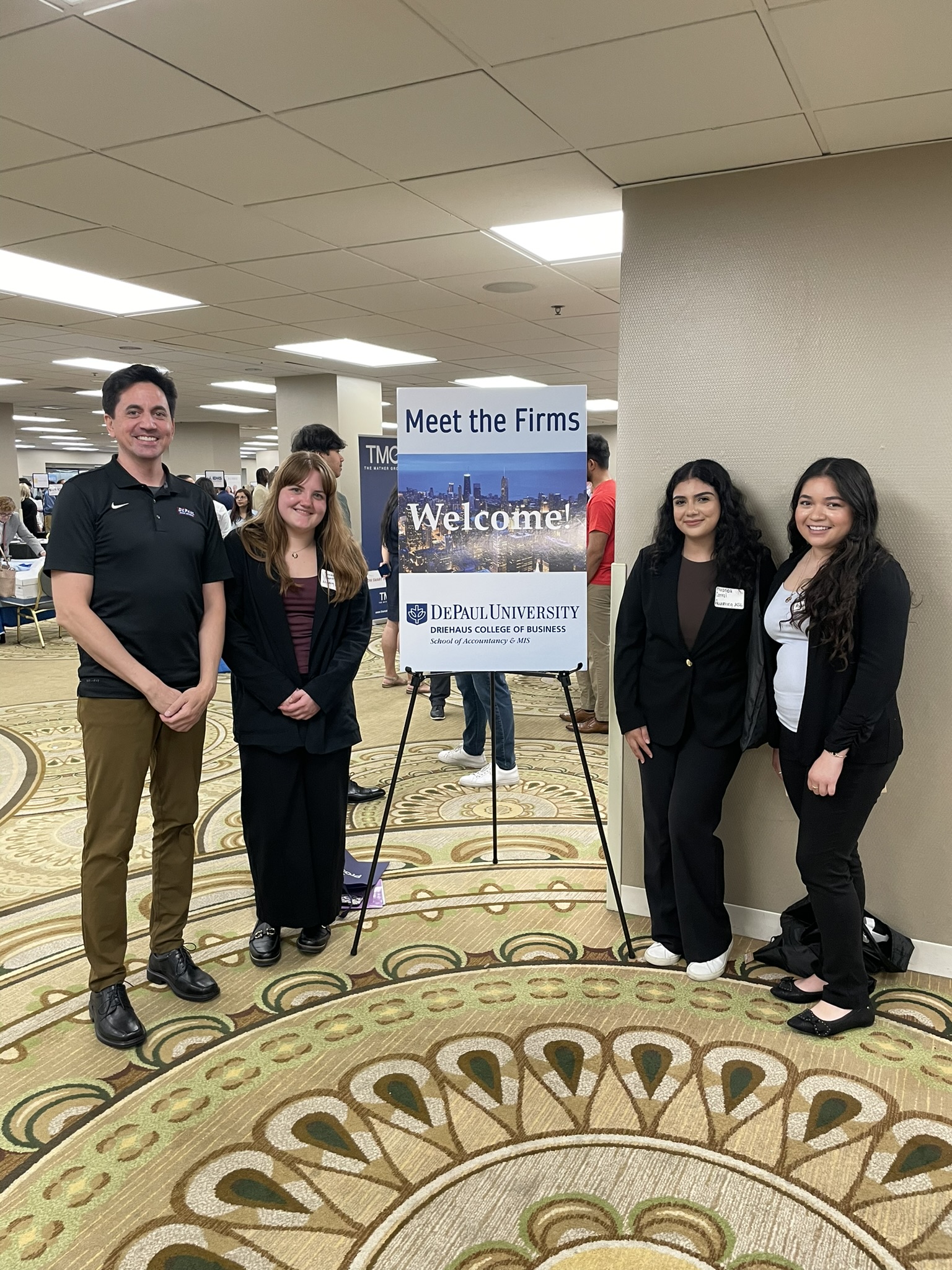 Three college students and a staff member pose in front of a sign that says 