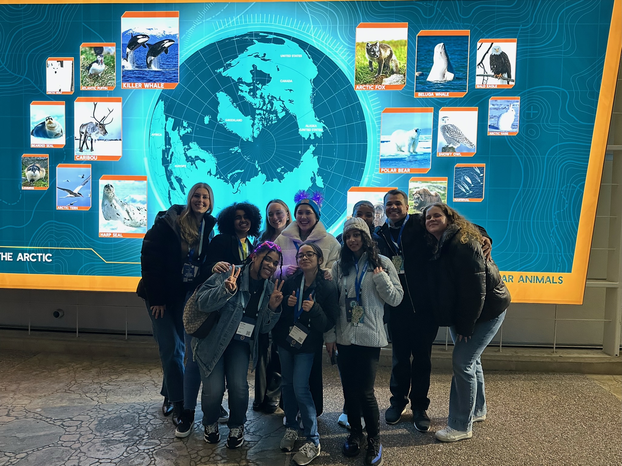 A group of students poses in front of a large display with an illuminated globe in the center