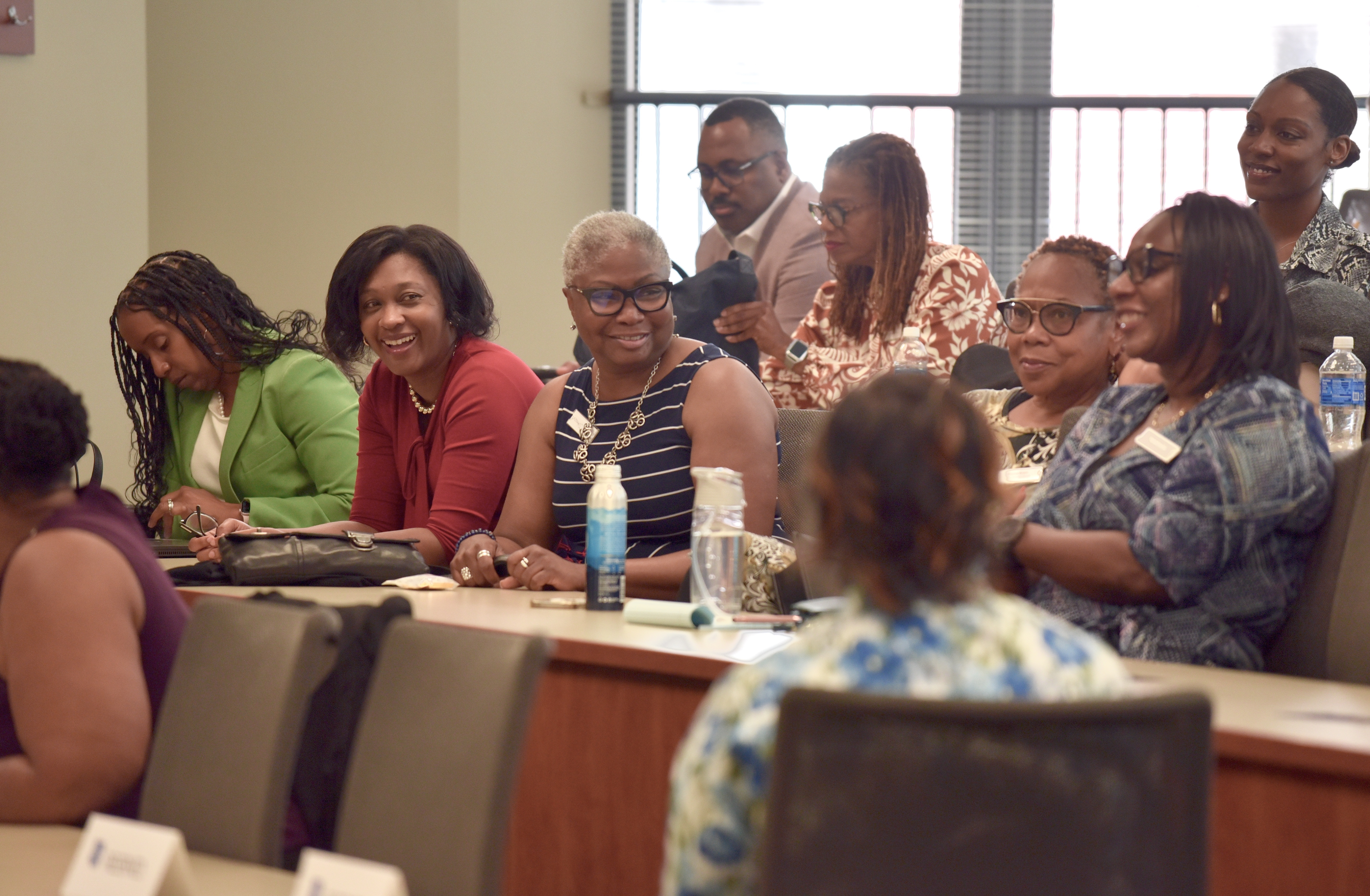 A group of people in business casual attire lean in, laughing, from their seats in a small lecture hall