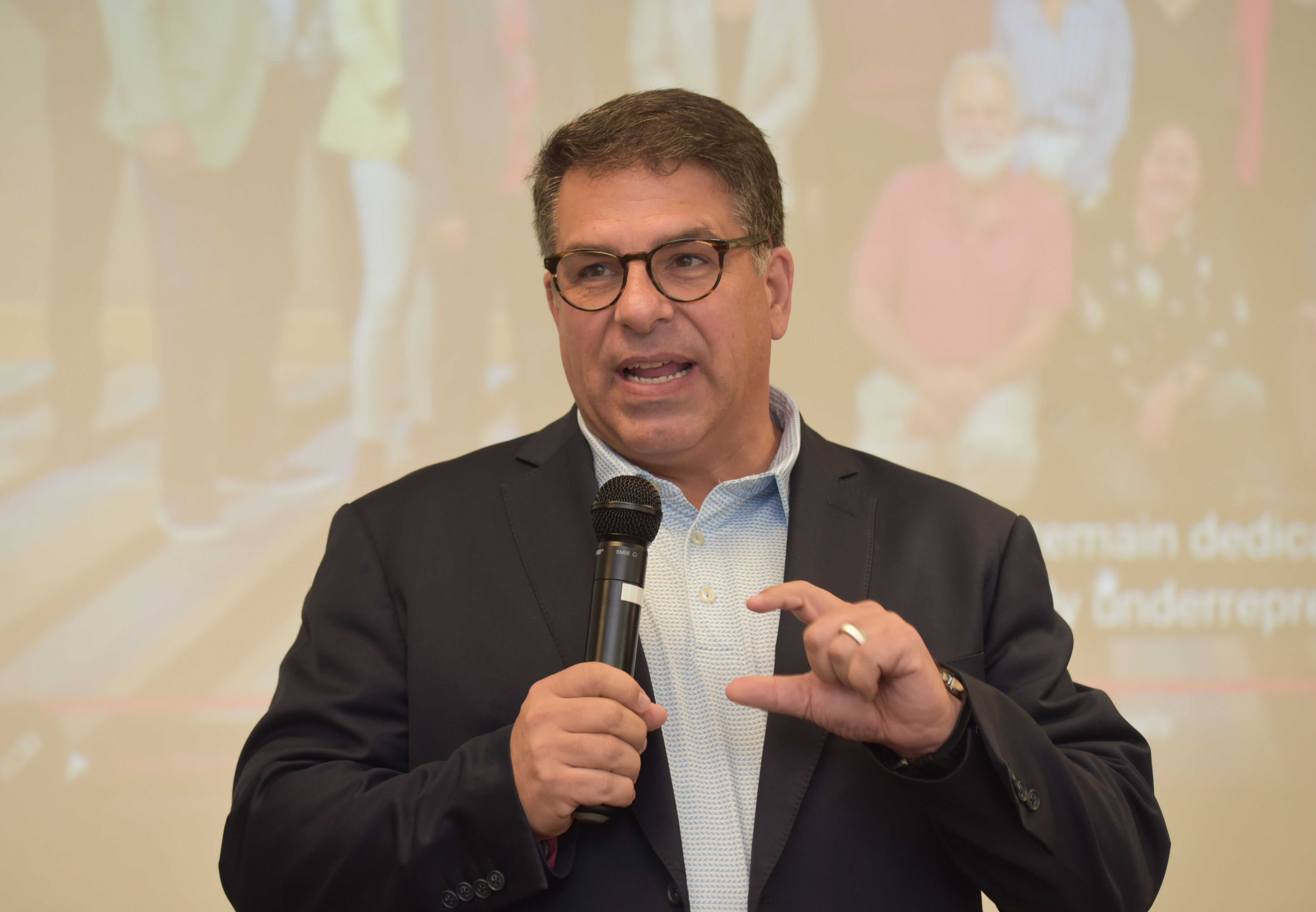 A middle-aged man in a suit speaks into a microphone